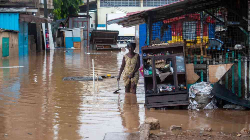 An older woman walking in a street flooded up to her knee in Accra, Ghana in 2020