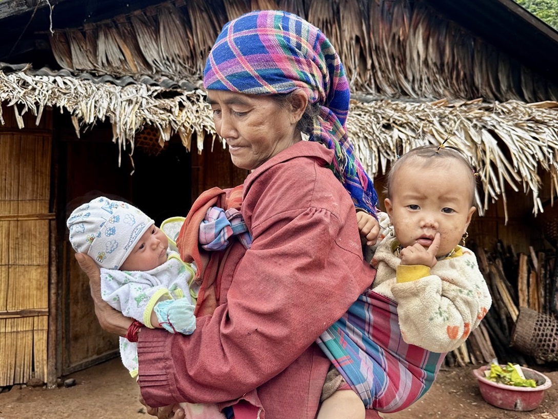 Woman holding two children in a Laotian village