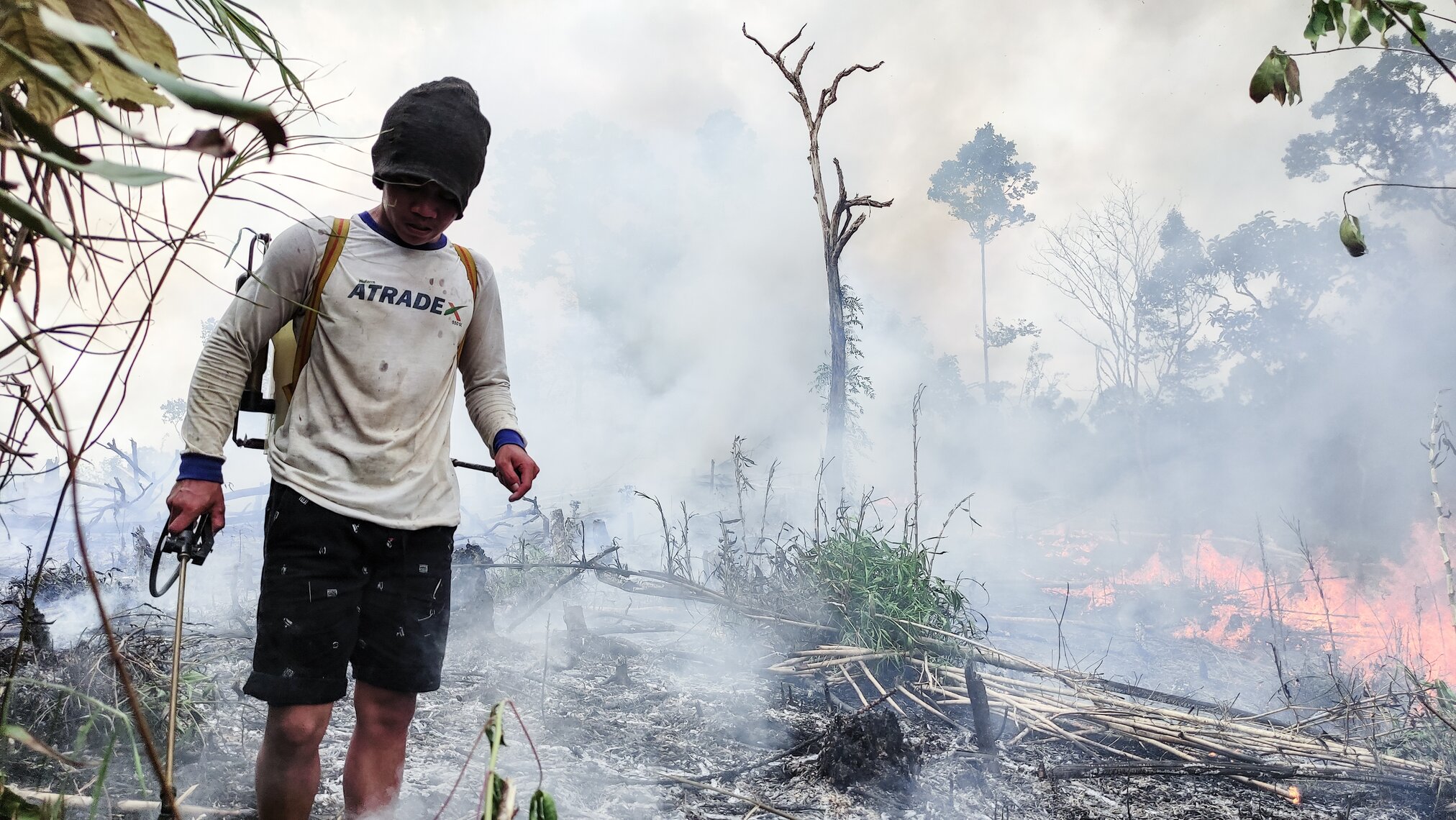 Borneo, Indonesia - August, 6th 2023: a local man holding a sprayer and extinguishing fire on a burning forest in Kalimantan, Indonesia.